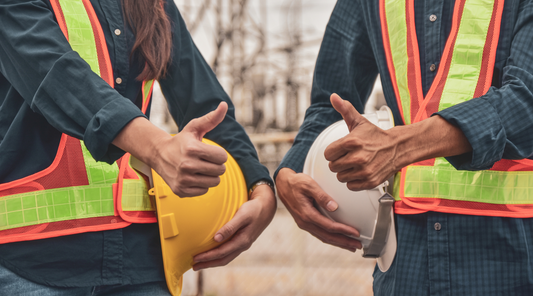 two workers holding hard hats giving the thumbs up sign