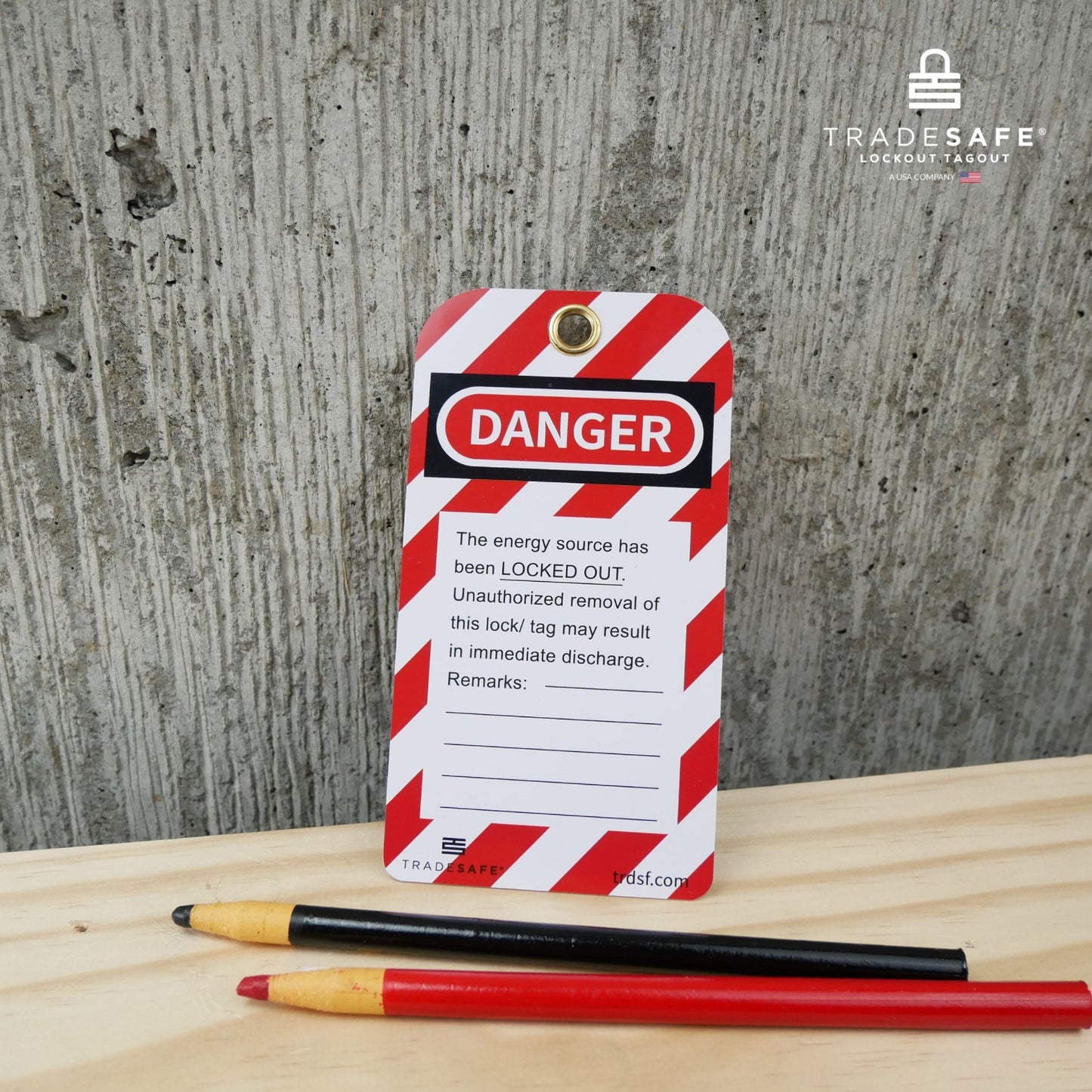 eye level view of a loto safety tag , black and red wax pencils placed on top of a table