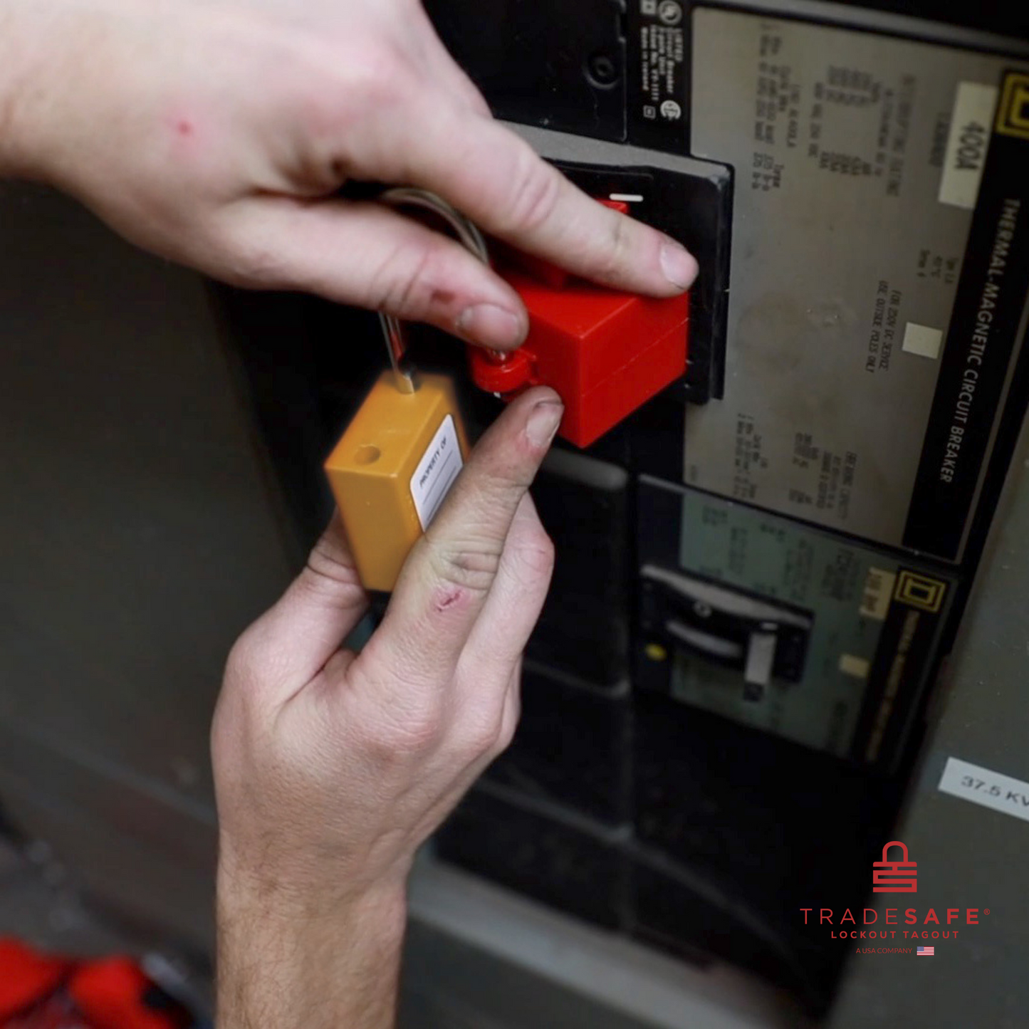 an orange loto padlock being inserted in a clamp-on circuit breaker lock