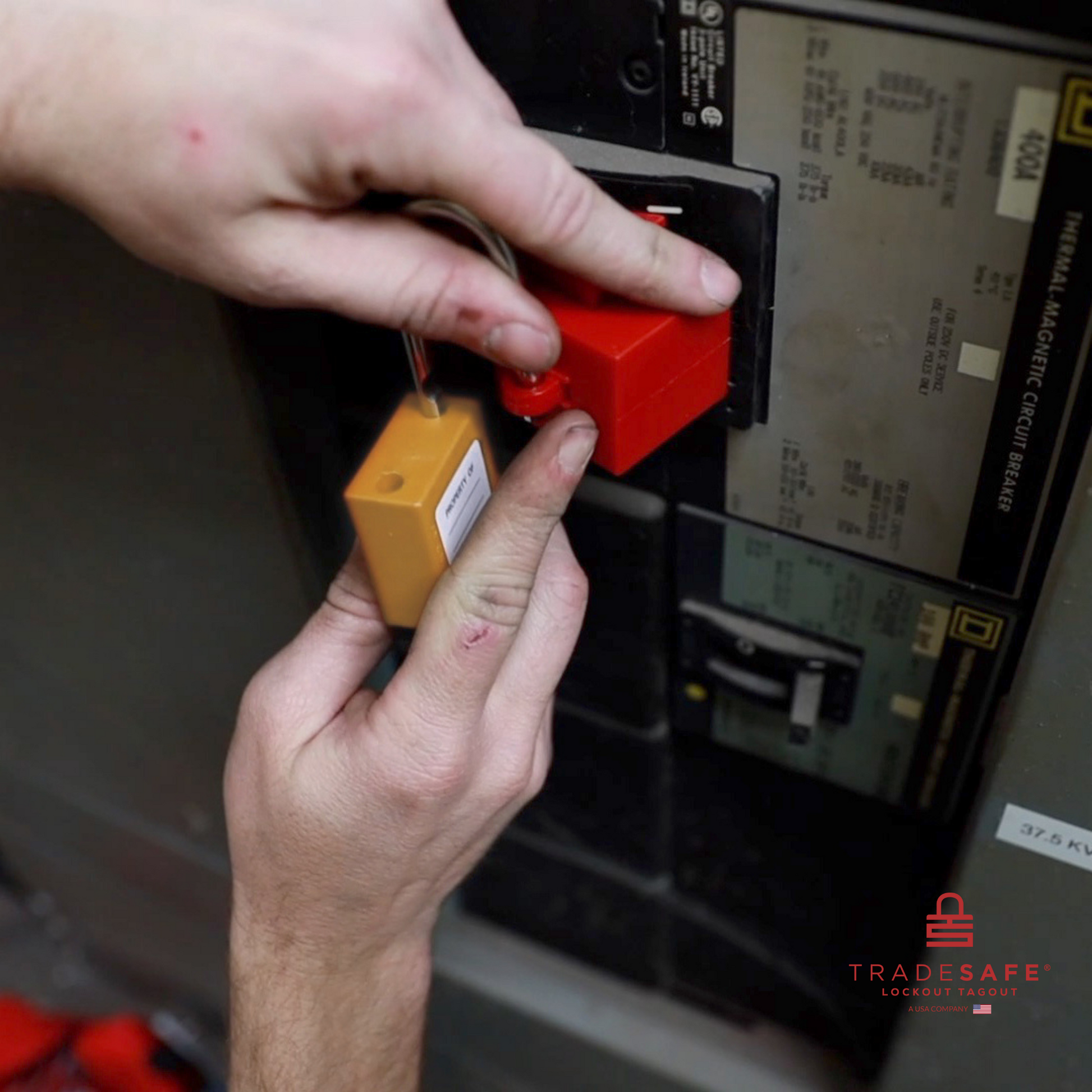 a orange loto padlock being inserted in a clamp-on circuit breaker lock